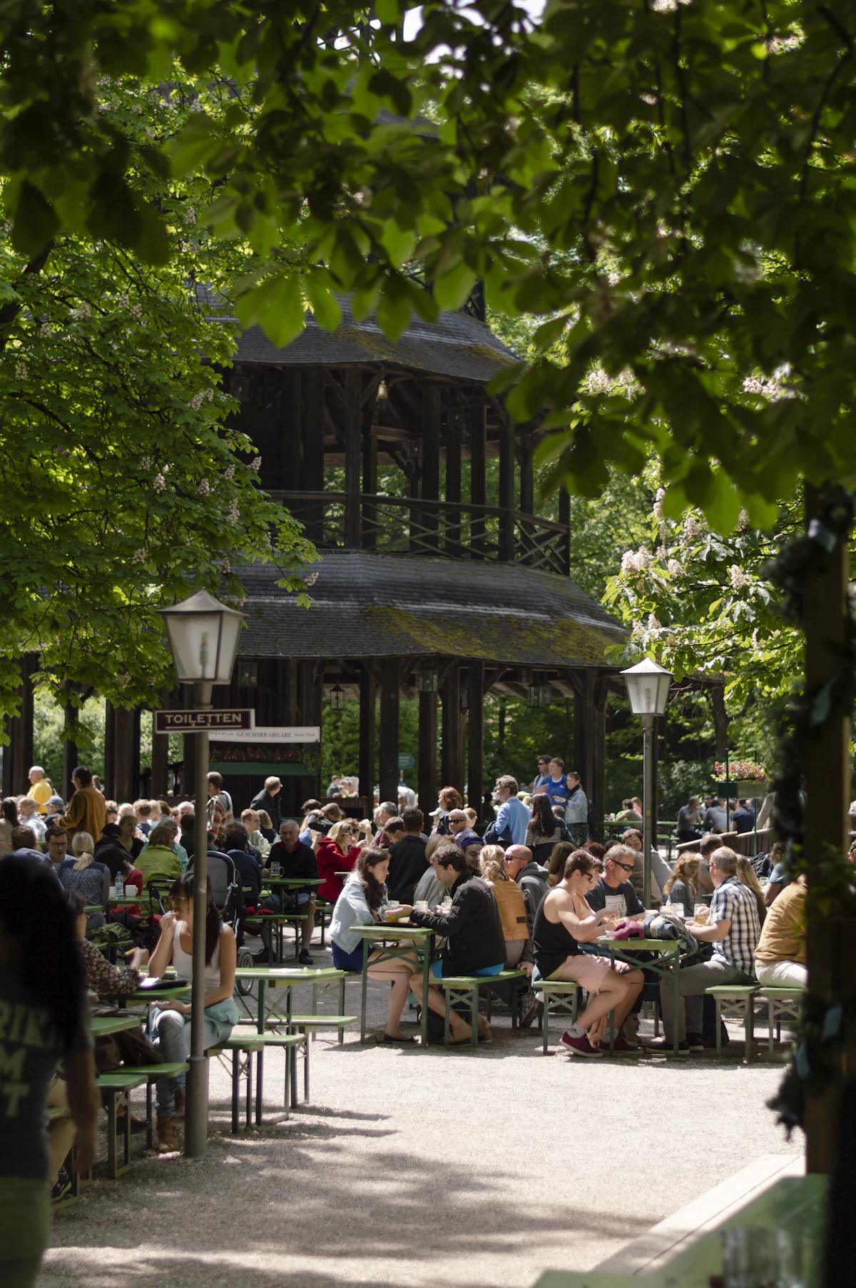 Gäste im Biergarten unter grünen Bäumen, tagsüber